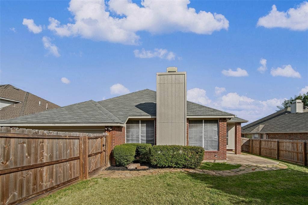714 Cottonwood Bend Drive, Allen, TX 75002 Exterior rear elevation featuring brick siding, a tall chimney, shingle roofing, and a flagstone pathway leading to a concrete patio enclosed by a wood privacy fence