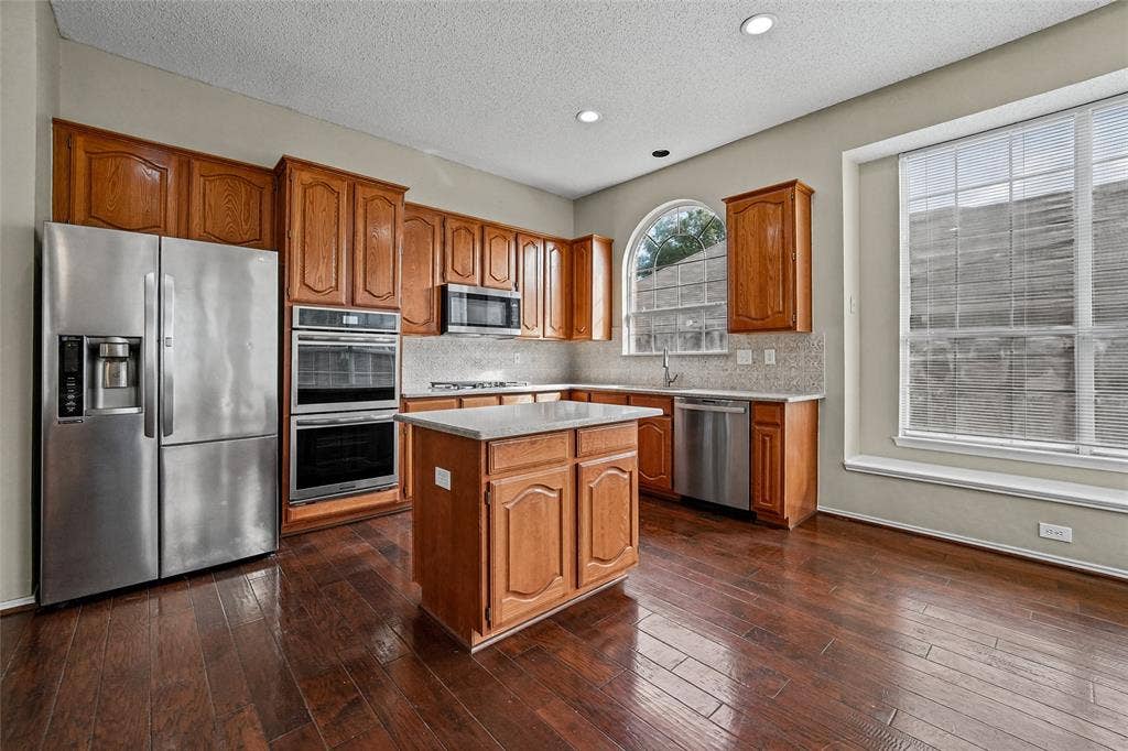 714 Cottonwood Bend Drive, Allen, TX 75002 Kitchen featuring wood cabinetry, stainless steel appliances, central island, arched window, and wood-finish flooring