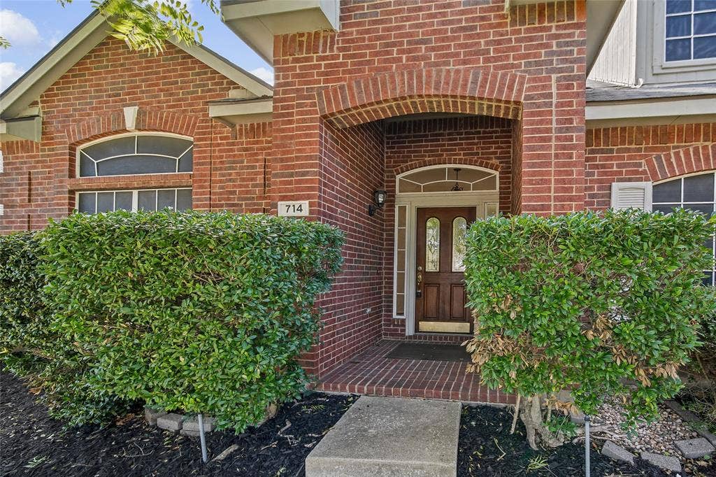 714 Cottonwood Bend Drive, Allen, TX 75002 Red brick exterior featuring an arched entryway, recessed porch, wood-paneled door with glass inserts, and decorative transom windows