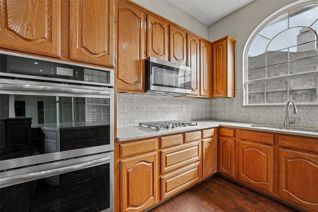 714 Cottonwood Bend Drive, Allen, TX 75002 Kitchen featuring wood cabinetry, stainless steel built-in double ovens, gas cooktop, arched window, and wood-finish flooring