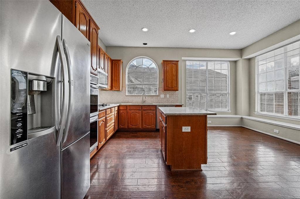 714 Cottonwood Bend Drive, Allen, TX 75002 Kitchen featuring wood cabinetry, stainless steel double wall ovens, a central island, recessed lighting, and an arched window