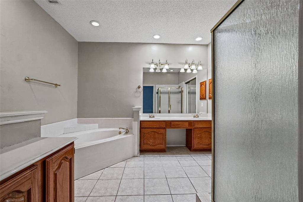 714 Cottonwood Bend Drive, Allen, TX 75002 Bathroom featuring wood-finish cabinetry, a large soaking tub with tile surround, a double-sink vanity, recessed lighting, and tile flooring