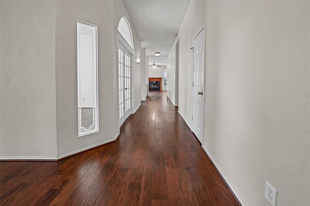 714 Cottonwood Bend Drive, Allen, TX 75002 Interior hall featuring wood-finish flooring, white French doors with an arched transom, a vertical accent window, and a built-in fireplace with a mantel