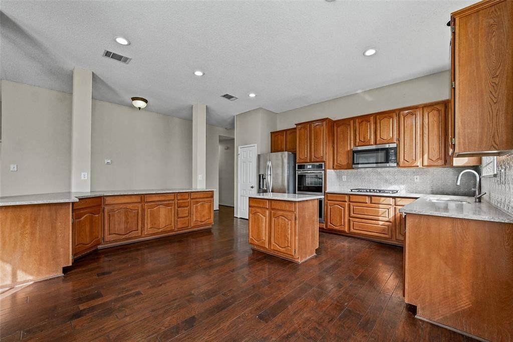 714 Cottonwood Bend Drive, Allen, TX 75002 Kitchen featuring stained wood cabinetry, stone countertops, a center island, stainless steel wall-mounted oven and microwave, and wood-finish flooring