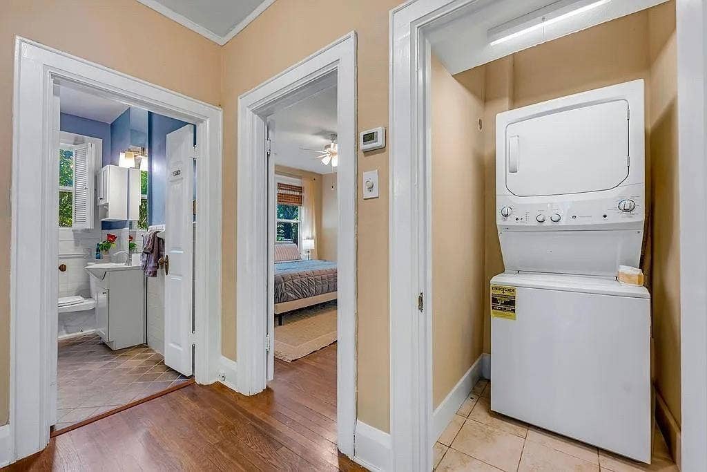 Hallway featuring wood-finish flooring, white door casings, and a built-in laundry closet with a stacked washer and dryer unit