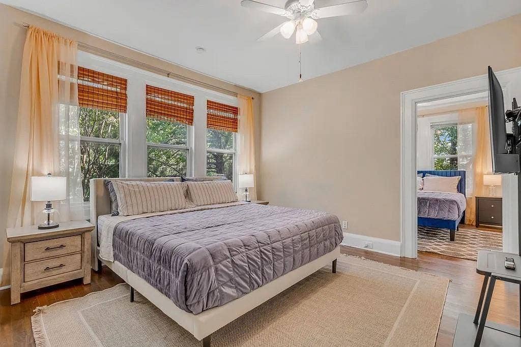 Spacious room featuring wood-finish flooring, a ceiling fan with integrated lighting, and a bank of three large windows