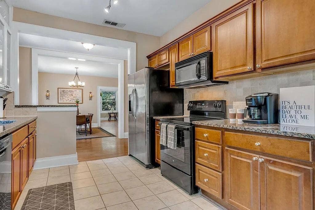 Kitchen featuring stained wood cabinetry, stone-finish countertops, tile flooring, and stainless steel appliances