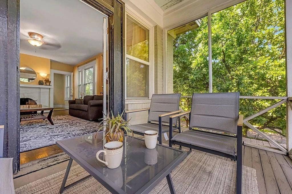 Screened-in porch featuring wood-plank flooring, cross-buck railing, and direct access to an interior living area with a fireplace and white mantel