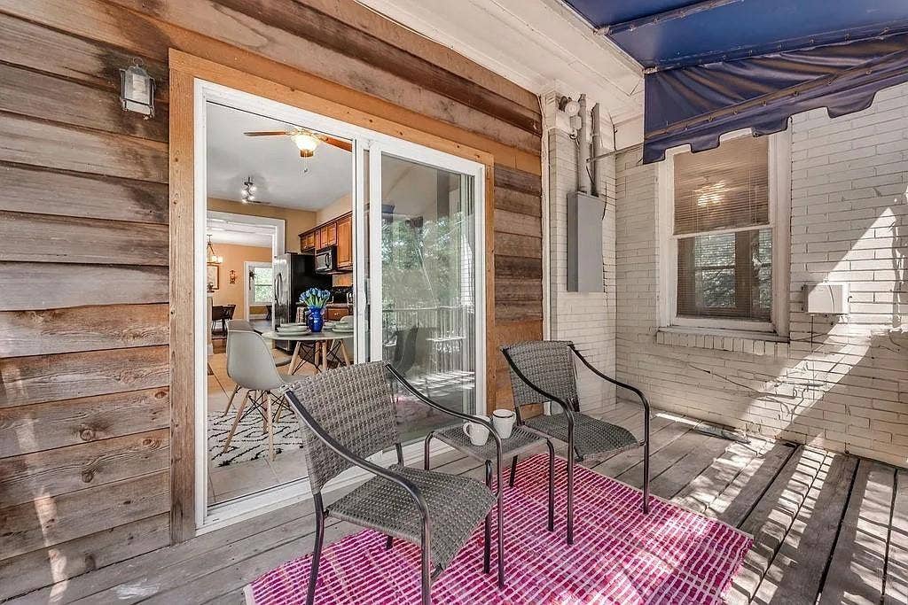 Covered patio featuring horizontal wood siding, white-painted brick masonry, a retractable blue awning, and a sliding glass door entry