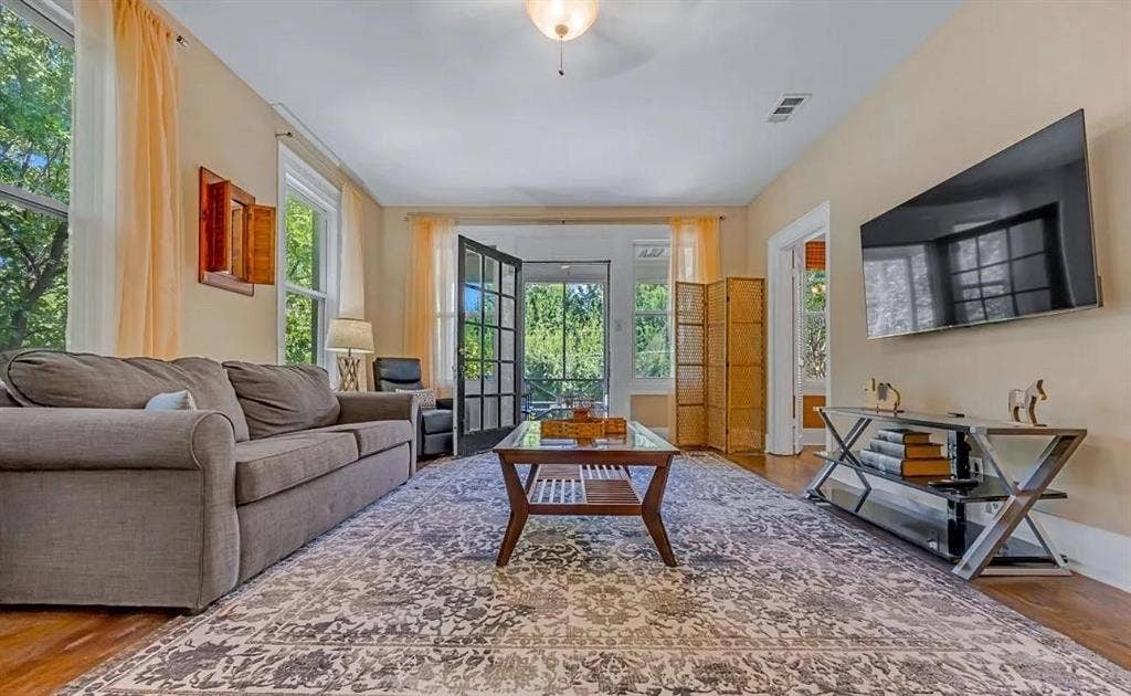 Living area featuring wood-finish flooring, high ceilings with central lighting, and multi-pane glass door access to a screened porch