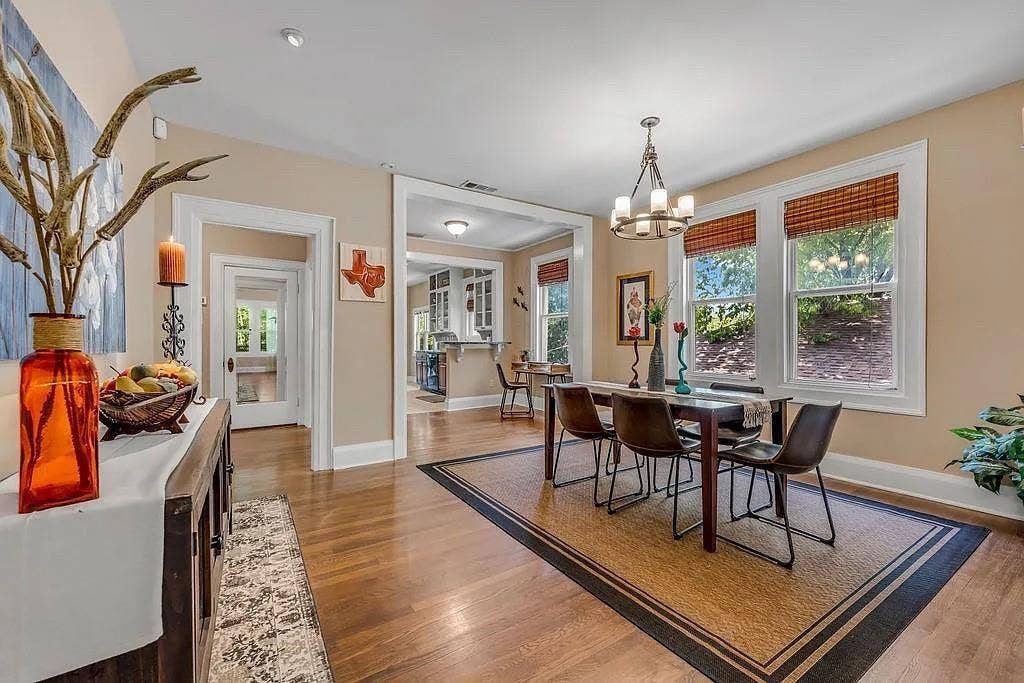 Dining area featuring wood-finish flooring, tall windows with woven shades, a multi-arm chandelier, and wide casing trim around openings