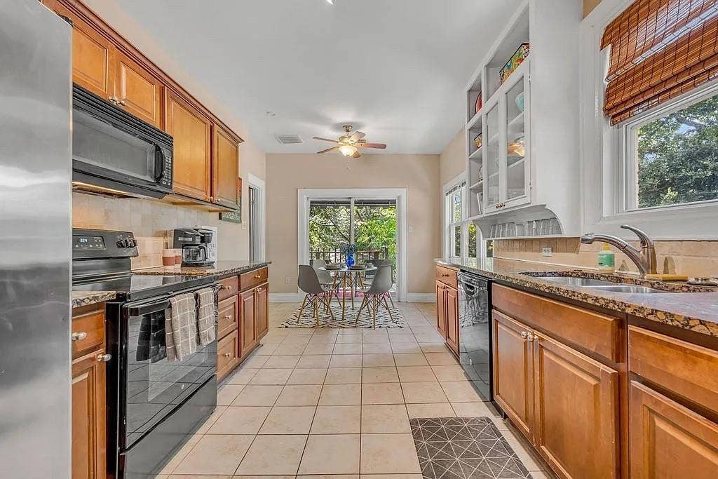 Kitchen featuring stained cabinetry, stone countertops, tile flooring, glass-front upper storage, and sliding glass doors