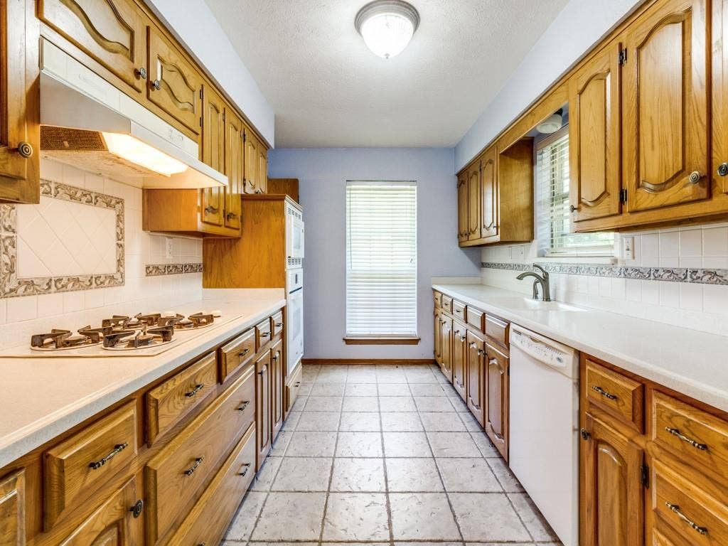 2007 Mistletoe Drive, Richardson, TX 75081 Kitchen with white appliances, under cabinet range hood, tasteful backsplash, baseboards, and a textured ceiling