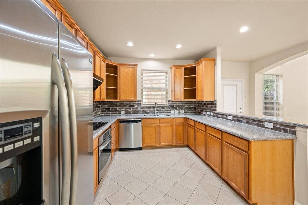 1712 Coronado Street, Allen, TX 75013 Kitchen featuring wood cabinetry, stone-surface countertops, brick-style tile backsplash, stainless steel appliances, and tile flooring