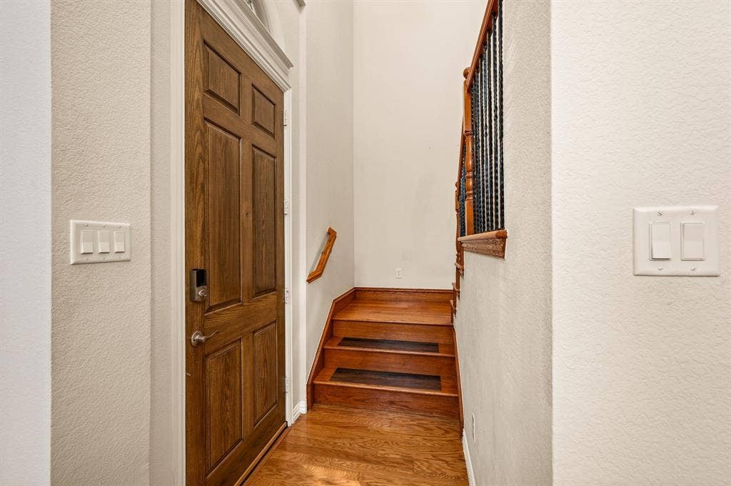 1712 Coronado Street, Allen, TX 75013 Entryway featuring a solid wood door, wood-finish flooring, wood staircase treads, and decorative wrought iron balusters