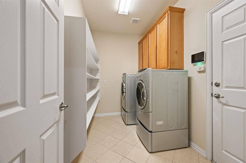1712 Coronado Street, Allen, TX 75013 Dedicated utility space featuring light-toned tile flooring, built-in wooden cabinetry, expansive open shelving, and a ceiling-mounted light fixture