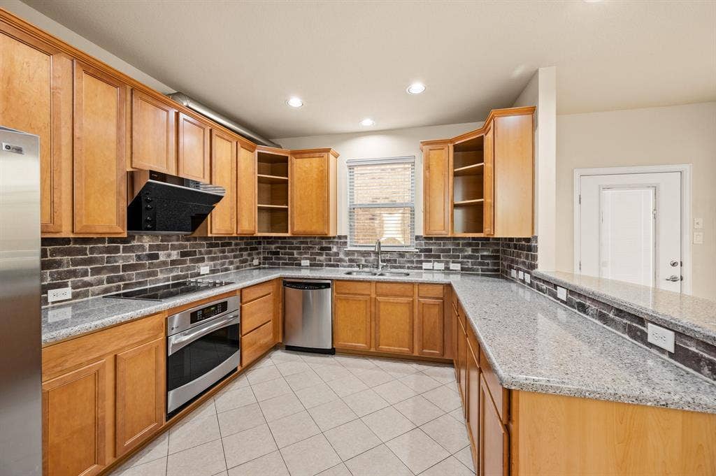 1712 Coronado Street, Allen, TX 75013 Kitchen featuring wood cabinetry, stone countertops, brick-style backsplash, stainless steel appliances, and tile flooring
