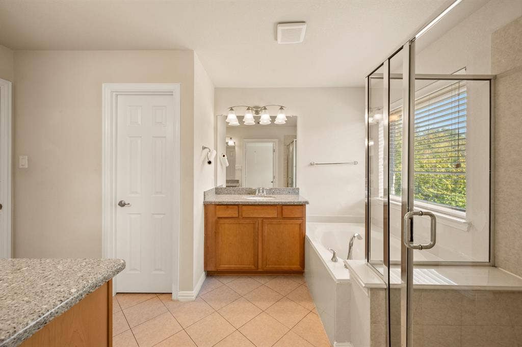 1712 Coronado Street, Allen, TX 75013 Bathroom featuring wood-finish cabinetry, stone-composite countertop with an integrated sink, glass-enclosed shower, soaking tub, and ceramic tile flooring