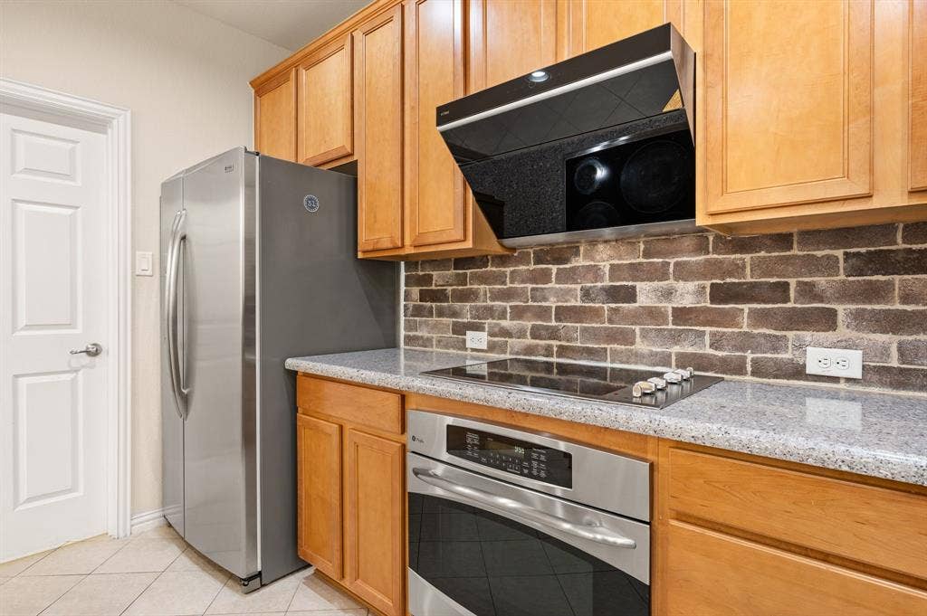 1712 Coronado Street, Allen, TX 75013 Kitchen featuring wood cabinetry, stone-finish countertops, stainless steel appliances, and a textured brick backsplash