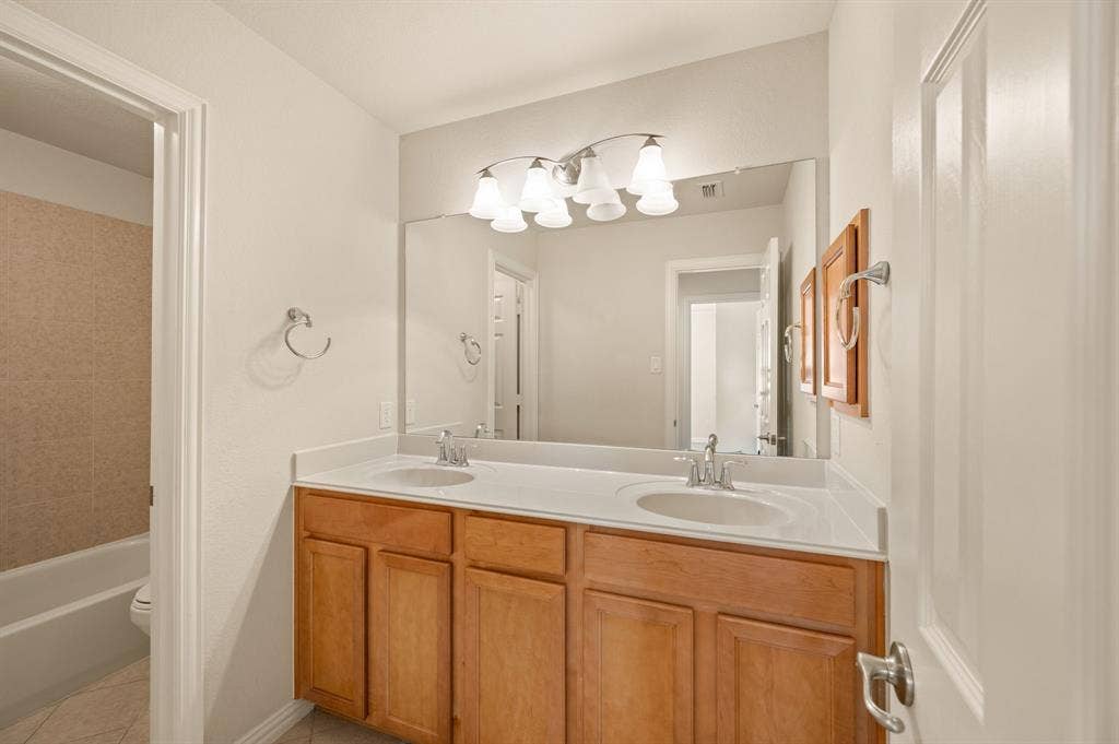 1712 Coronado Street, Allen, TX 75013 Bathroom featuring a double-sink vanity with wood cabinetry, a solid-surface countertop, an expansive wall-mounted mirror, and multi-bulb decorative lighting