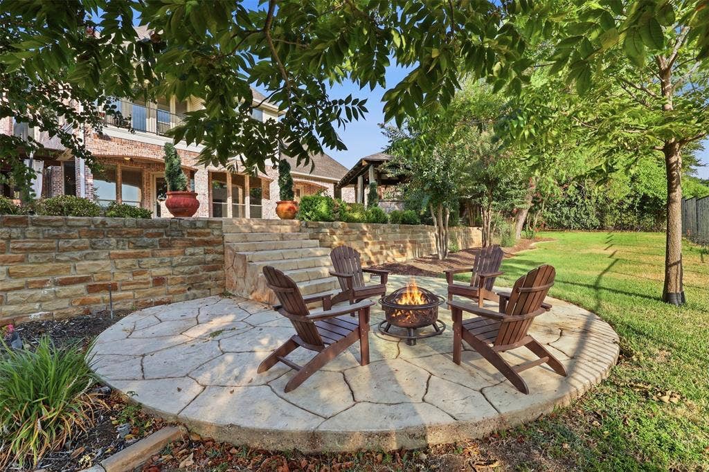 1919 Kings Pass, Heath, TX 75032 Stone-retained patio featuring a circular flagstone hardscape, multiple mature trees, and a tiered stone staircase leading to the residence
