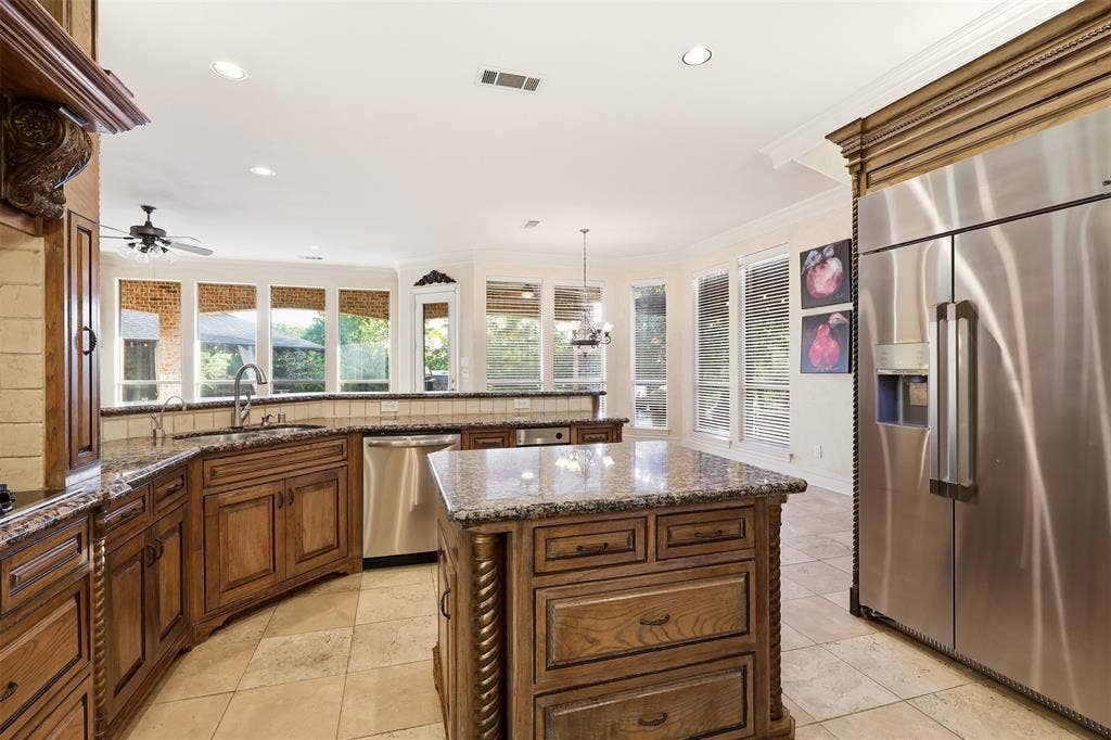 1919 Kings Pass, Heath, TX 75032 Kitchen featuring stone tile flooring, granite countertops, wood cabinetry, a center island with storage, and a stainless steel refrigerator