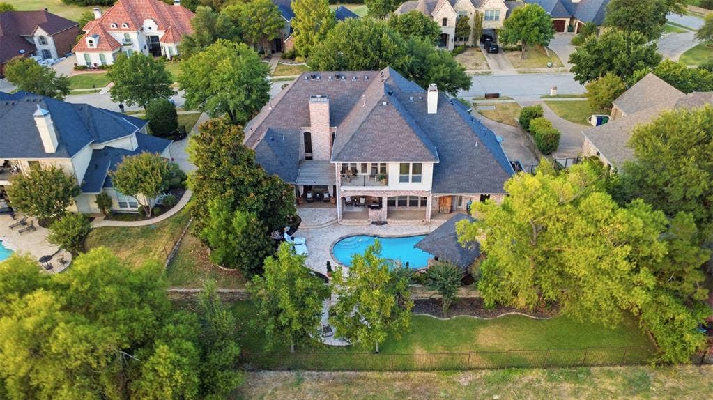 1919 Kings Pass, Heath, TX 75032 Expansive rear exterior featuring a swimming pool, covered patio, second-story balcony, and mature trees. This home backs up to the green belt for privacy. The custom details enhances the view as the sun sets around it.