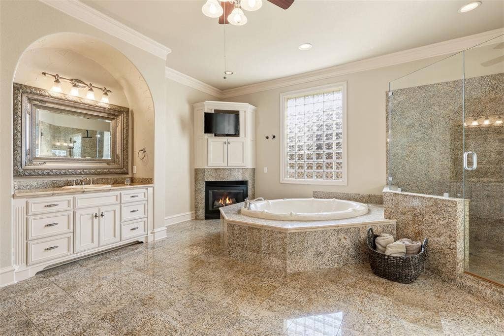 1919 Kings Pass, Heath, TX 75032 Spacious bathroom featuring a jetted tub with polished chrome fixtures, a walk-in shower with glass enclosure and tiled surround, a vanity with ample storage and a framed mirror, and light-toned tile flooring