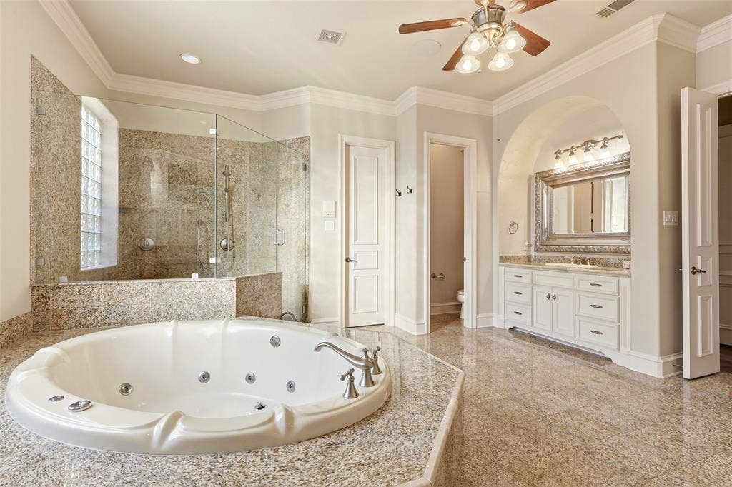1919 Kings Pass, Heath, TX 75032 Spacious bathroom featuring a jetted tub with polished chrome fixtures, a walk-in shower with glass enclosure and tiled surround, a vanity with ample storage and a framed mirror, and light-toned tile flooring