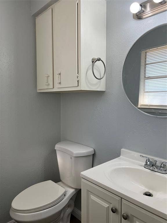 102 Silver Creek Drive, Duncanville, TX 75137 Bathroom featuring a white vanity cabinet with an integrated basin, brushed nickel hardware, a circular wall-mounted mirror, and a wall-mounted storage cabinet