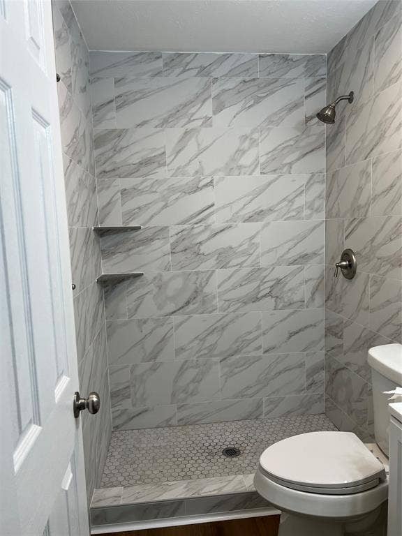 102 Silver Creek Drive, Duncanville, TX 75137 Shower enclosure featuring full-height large-format stone-patterned wall tile, hexagonal floor tile, two built-in corner shelves, and a metal shower head with matching pressure-balance valve