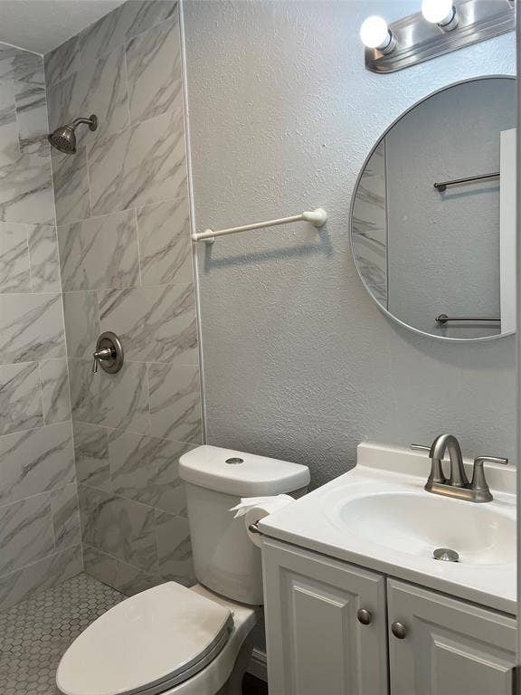 102 Silver Creek Drive, Duncanville, TX 75137 Bathroom featuring a walk-in shower with large-format tile surround, hexagonal floor tiling, white vanity with integrated sink, and round wall-mounted mirror