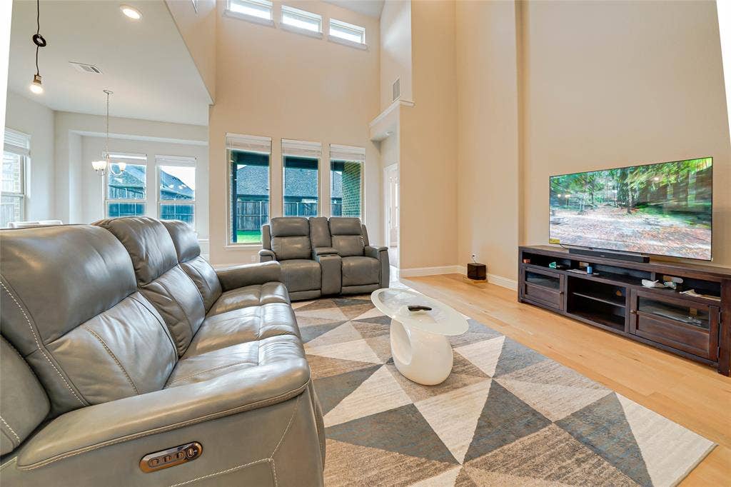 Living room with light wood-style flooring, recessed lighting, and a towering ceiling