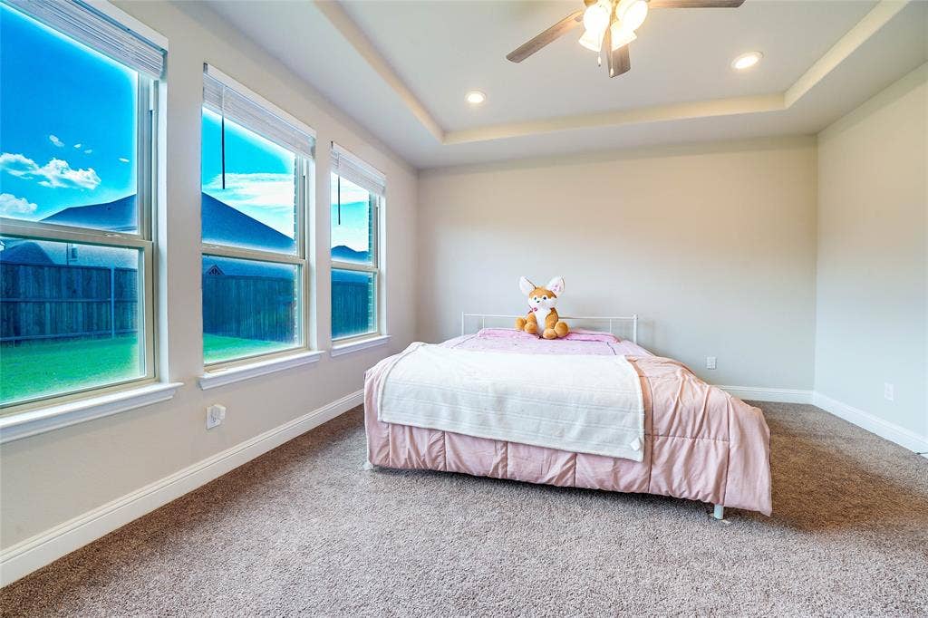 Carpeted bedroom featuring a tray ceiling, ceiling fan, and recessed lighting