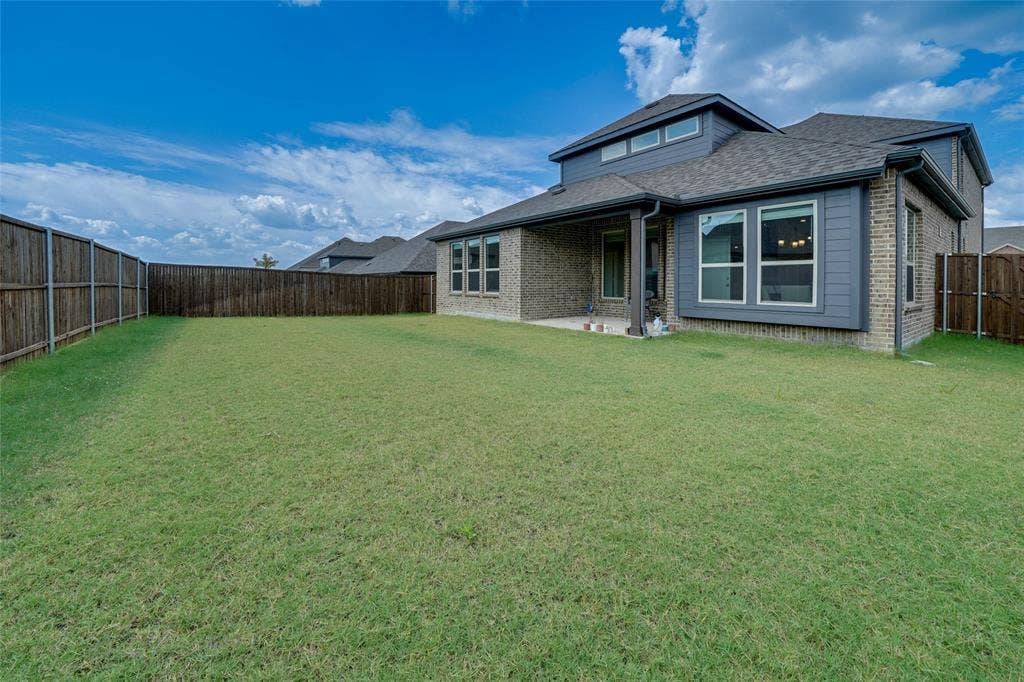 Back of house with brick siding, a patio, a fenced backyard, and roof with shingles