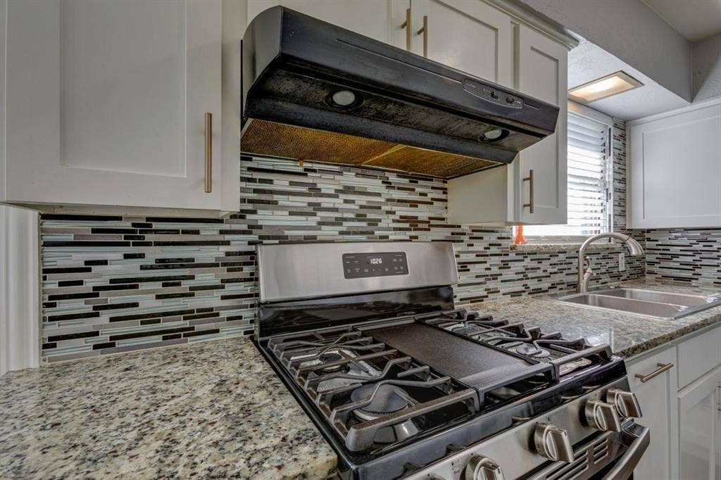 1600 Summit Street, Mesquite, TX 75149 Kitchen featuring white cabinetry with brushed metal hardware, speckled stone countertops, a multi-tonal glass tile backsplash, and stainless steel gas range with a center griddle