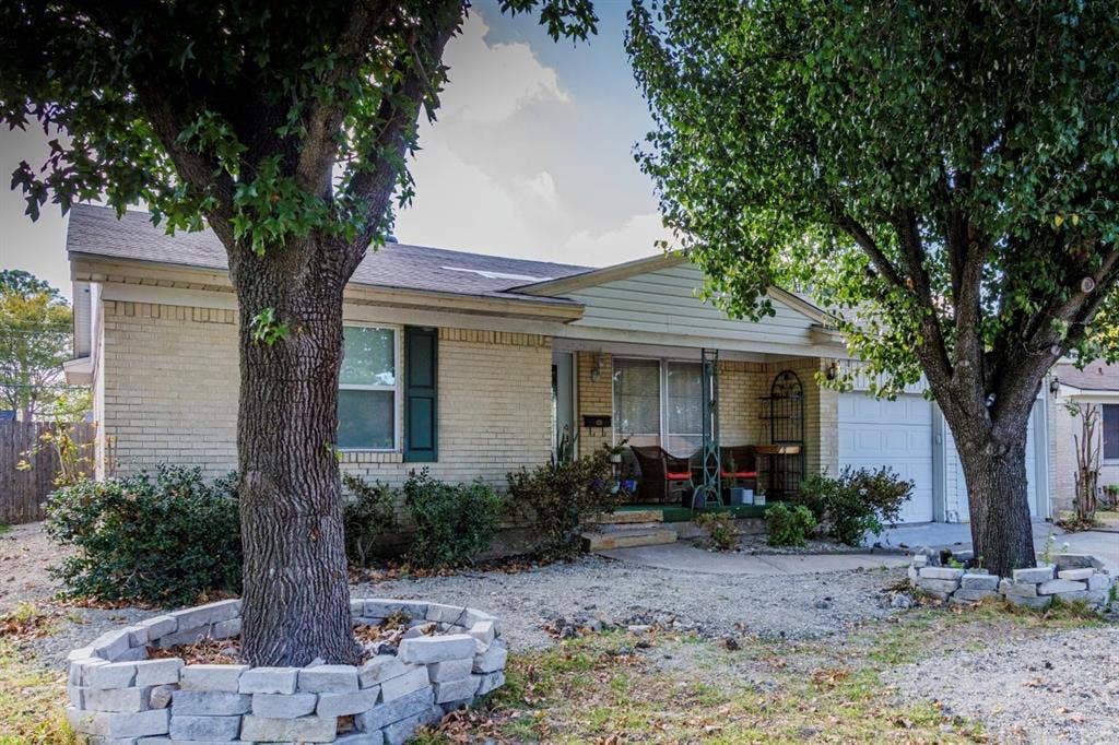 1600 Summit Street, Mesquite, TX 75149 Single-story exterior featuring light-toned brick masonry, gable roofline, attached garage, and stone tree rings