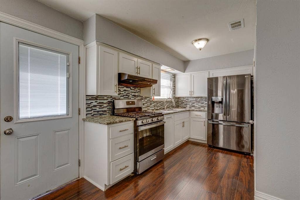 1600 Summit Street, Mesquite, TX 75149 Kitchen featuring white shaker-style cabinetry, stone-finish countertops, decorative multi-tone tile backsplash, stainless steel appliances, and wood-finish flooring