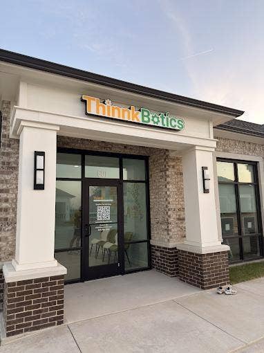 Exterior facade featuring masonry brickwork, a covered entryway with structural columns, and large-format glass storefront windows with black framing