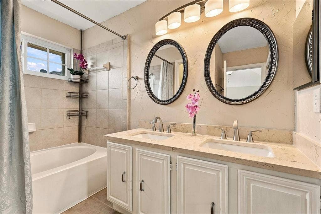 2524 Brooke Trail, Carrollton, TX 75006 Dual-sink vanity with stone-finish countertop, oval wall-mounted mirrors, light-finish cabinetry with metallic hardware, and a tile-surround soaking tub