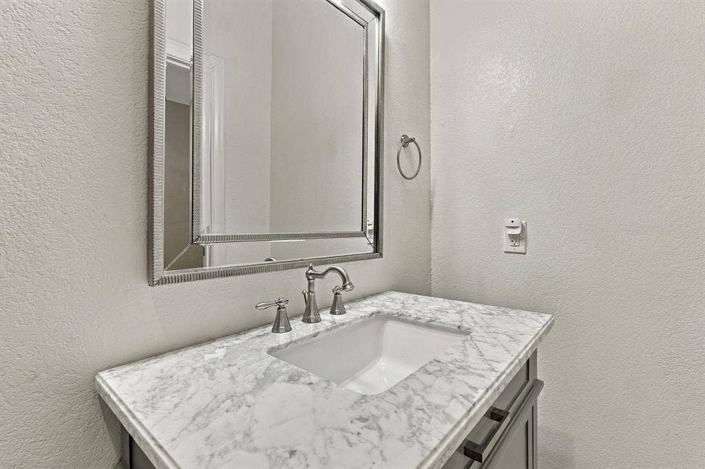 510 E Malone Street, Celina, TX 75009 Stone-surface vanity featuring an undermount sink, brushed-metal widespread faucet, and rectangular framed mirror