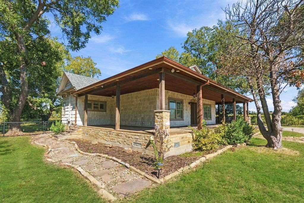 510 E Malone Street, Celina, TX 75009 Stone veneer exterior featuring a wraparound covered porch, exposed wood ceiling beams, stone support columns, and a flagstone pathway