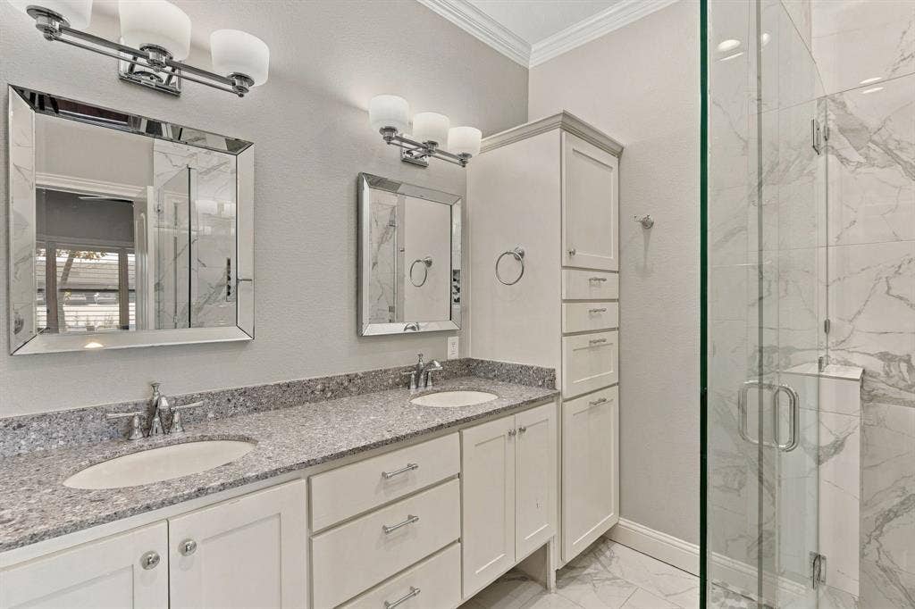 510 E Malone Street, Celina, TX 75009 Dual-sink vanity with stone-finish countertop, crisp white cabinetry with floor-to-ceiling storage, framed mirrors, multi-bulb vanity lighting, and walk-in shower with floor-to-ceiling tile surround