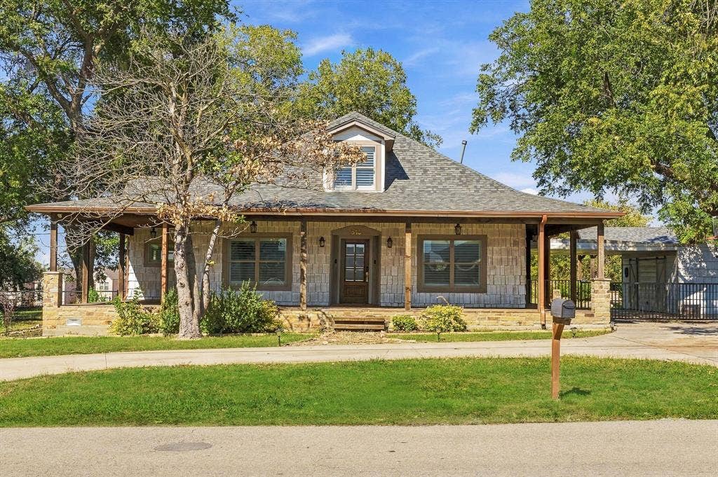 510 E Malone Street, Celina, TX 75009 Single-story residence featuring a light-toned stone exterior, wrap-around covered porch, dormer window, and shingled roof