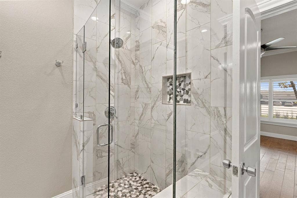 510 E Malone Street, Celina, TX 75009 Walk-in shower featuring floor-to-ceiling large-format tile, glass enclosure, built-in recessed niche with decorative stone inlay, and a pebble-stone tiled floor