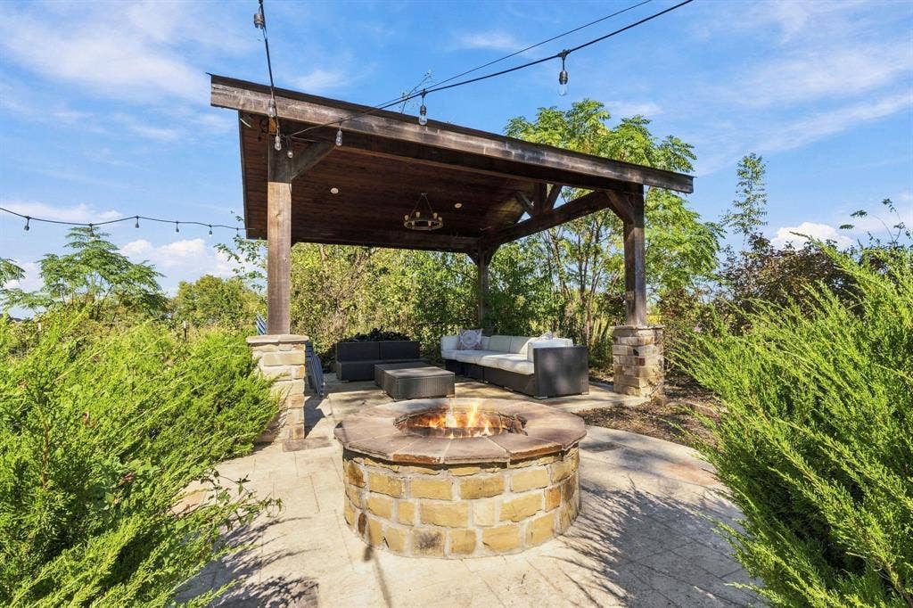 510 E Malone Street, Celina, TX 75009 Covered timber-frame pavilion with stone pillar bases, circular stone fire pit, paver patio, and overhead bistro-style lighting