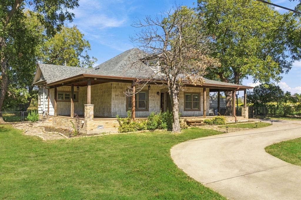 510 E Malone Street, Celina, TX 75009 Single-story residence featuring a stone veneer exterior, wraparound covered porch, stone column supports, shingle roof, and a paved driveway
