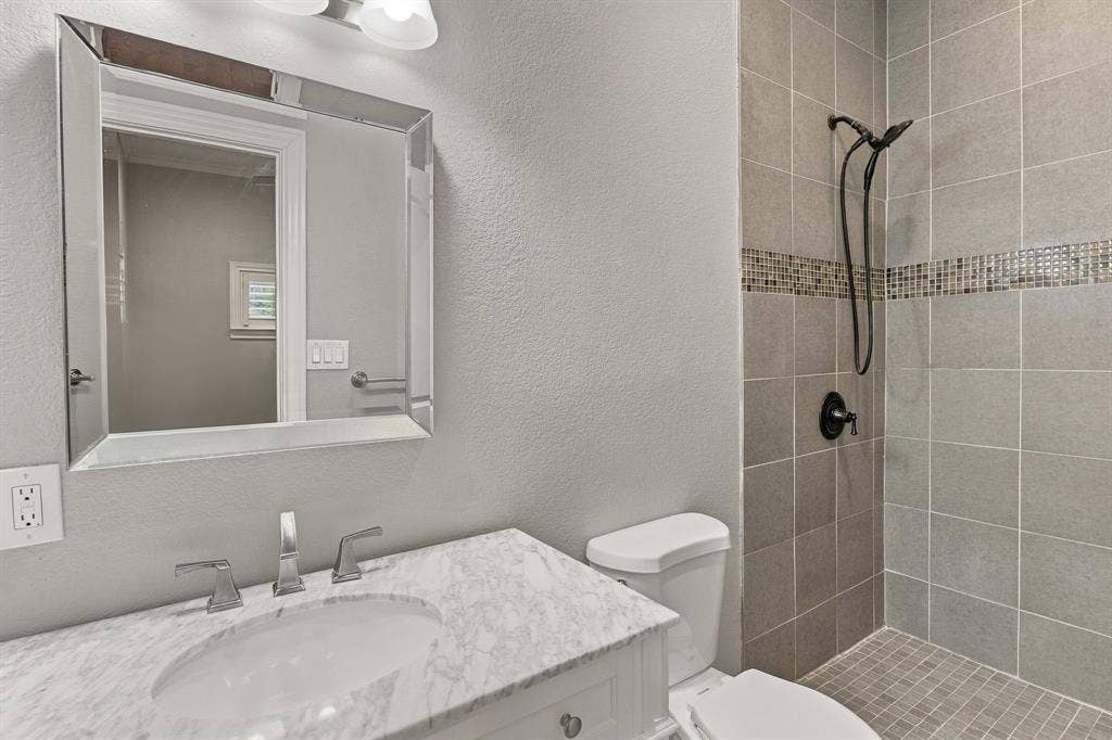 510 E Malone Street, Celina, TX 75009 Bathroom featuring a vanity with a stone countertop and undermount sink, a framed mirror, and a tiled shower with a decorative mosaic inlay and a matte black handheld showerhead