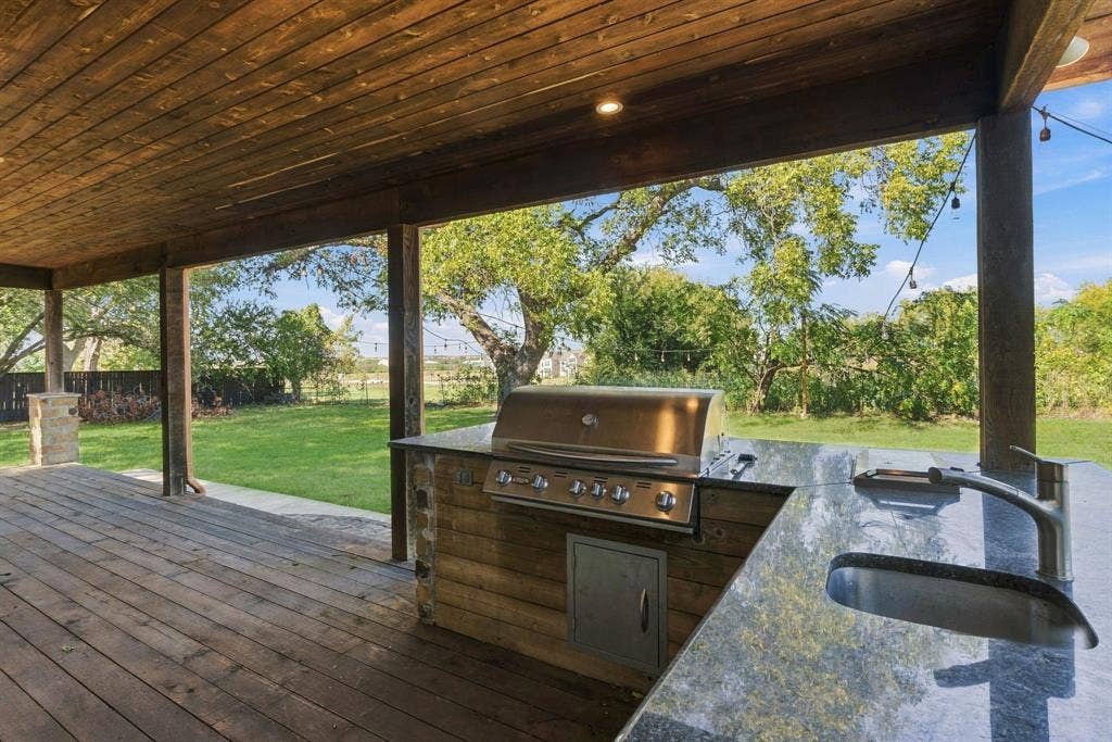 510 E Malone Street, Celina, TX 75009 Covered outdoor kitchen featuring wood-plank ceiling, stone-accented base, stainless steel grill, natural stone countertop, and undermount sink