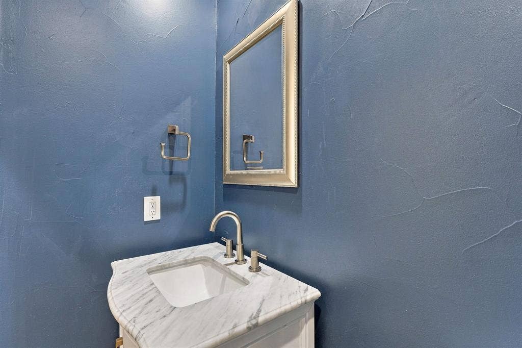 510 E Malone Street, Celina, TX 75009 Custom vanity with stone-top surface, undermount basin, brushed-nickel widespread faucet, framed wall-mounted mirror, and textured wall finish